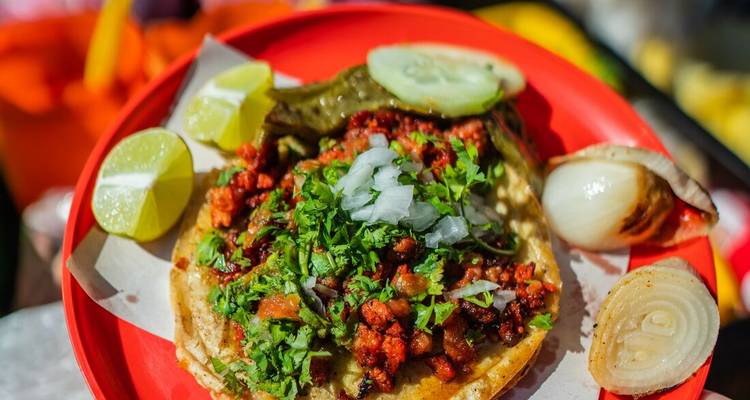Close-up of a taco with lime wedges on a red plate.