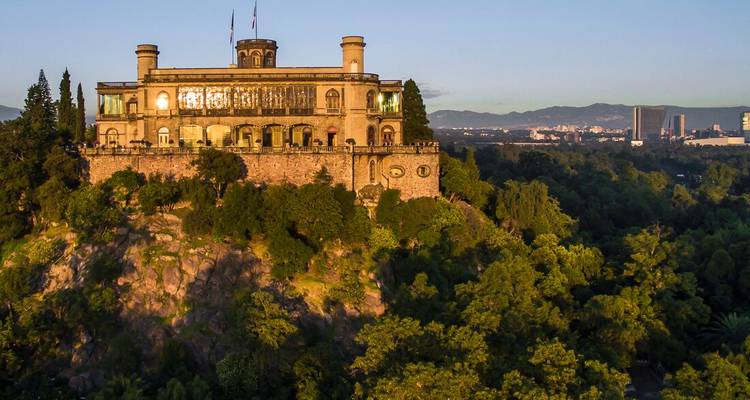 Aerial view of a historic hilltop castle surrounded by trees.