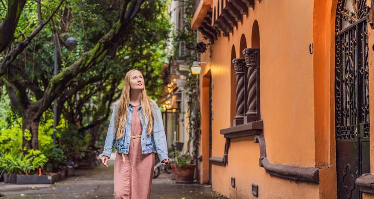 Woman walking by an orange building with greenery.