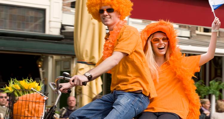 Menschen in orangefarbenen Kostümen fahren Fahrrad bei einem Festival in den Niederlanden.
