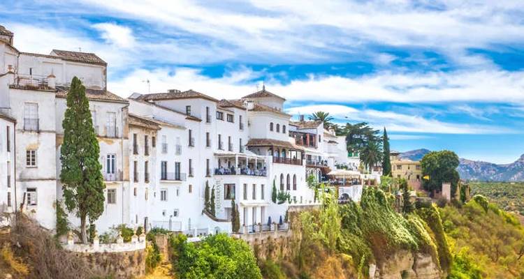 Las casas blancas en lo alto del acantilado de Ronda se asoman dramáticamente sobre un profundo desfiladero con colinas ondulantes al fondo.