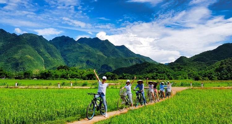 Group of cyclists in a green valley with blue sky mountains.
