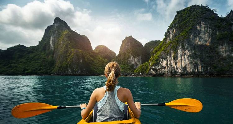 Woman kayaking in Ha Long Bay with limestone cliffs.