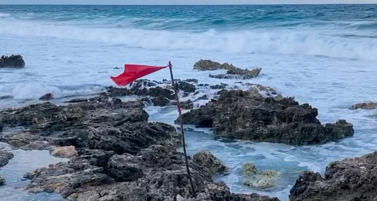 Rochers côtiers avec des vagues qui s'écrasent et un drapeau rouge.
