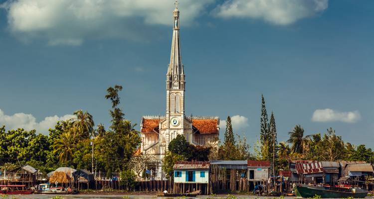 A riverside with a church surrounded by trees and houses.