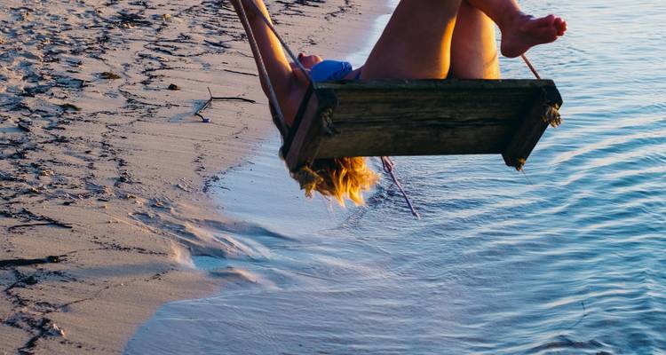 Person on a swing at the beach at sunset.