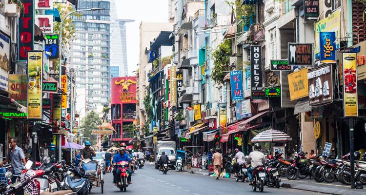 Busy city street with shops, motorcycles, and people.