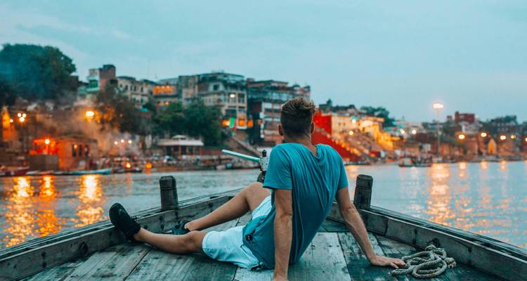 Man relaxing on a boat with a riverside view at twilight.