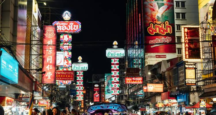 A bustling street in Bangkok with illuminated signs at night.