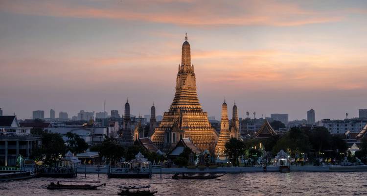 Wat Arun temple in Bangkok with a river in the foreground at sunset.