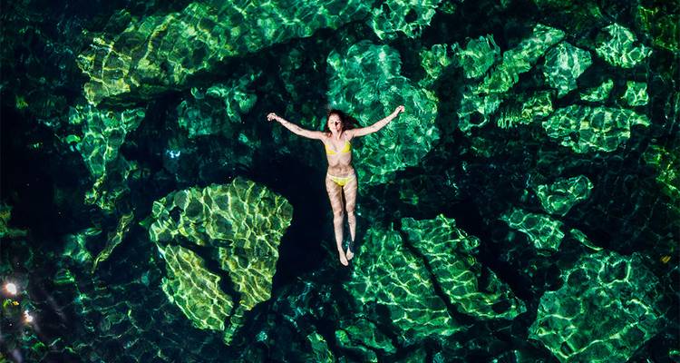 Person floating in clear water with stone formations