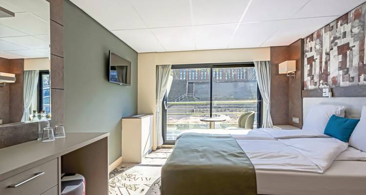 Interior of a cruise cabin with a bed, TV, and a large window.