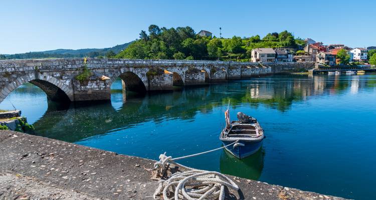 Pont historique en pierre au-dessus d'une rivière tranquille avec un petit bateau.