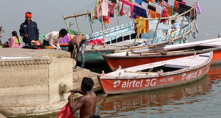People and boats on a river, with colorful fabric drying.