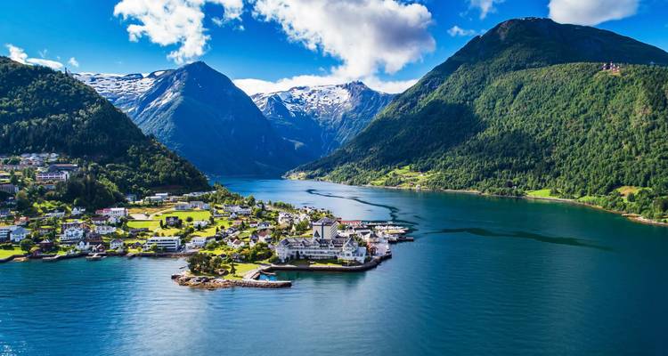 Village idyllique de fjord avec hôtel blanc et église nichés entre des montagnes d'émeraude et des eaux calmes.