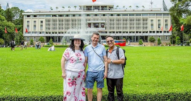Trois personnes posant devant un bâtiment gouvernemental avec des drapeaux.