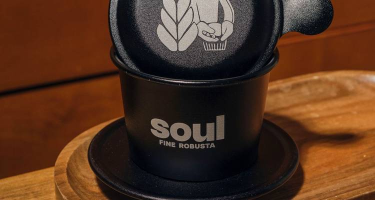 Une tasse noire avec les mots 'Soul Fine Robusta' dessus, posée sur une surface en bois.