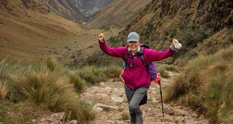A person hiking on a mountain trail, raising hands in joy.