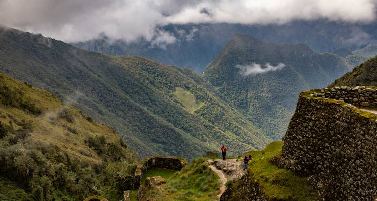 People hiking near ancient stone ruins with a mountain backdrop.