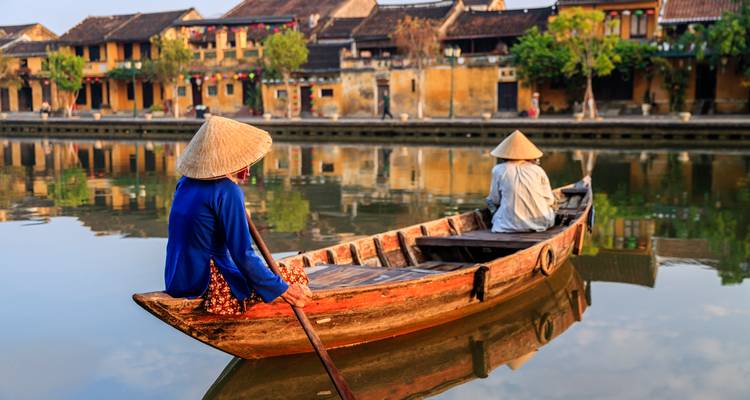 Des gens en tenues traditionnelles ramant sur une rivière dans un bateau.