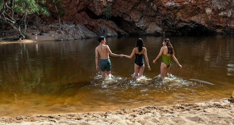 Le groupe s'avance dans un point d'eau calme entouré de parois rocheuses rouges et d'eucalyptus.