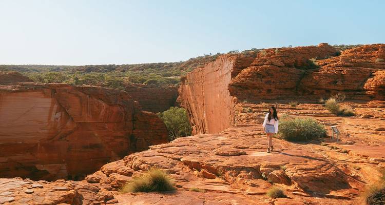 Une femelle randonneuse marchant le long de la crête du Kings Canyon aux roches rouges sous un ciel dégagé.