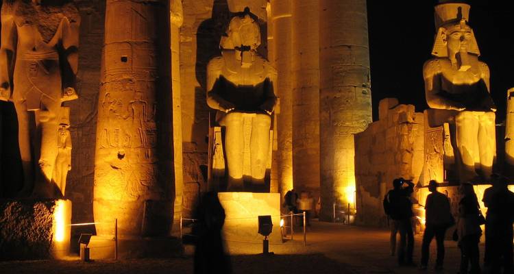 Illuminated colossal statues and pillars of Luxor Temple glowing against the dark night sky.