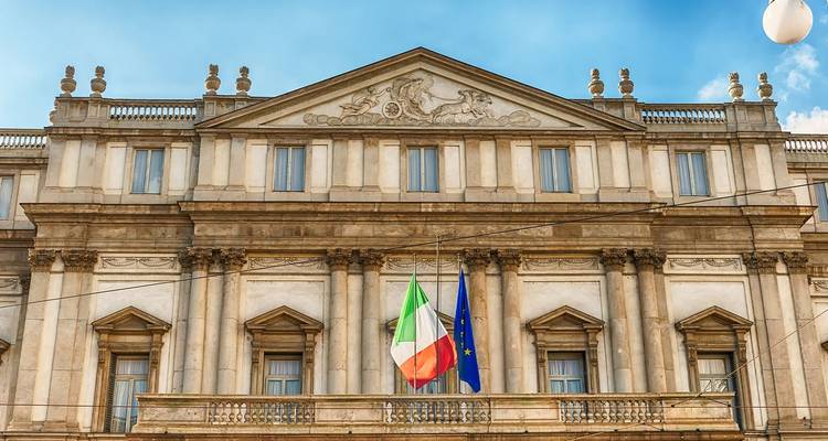 Façade néoclassique de l'opéra La Scala avec les drapeaux italiens et européens sur fond de ciel bleu