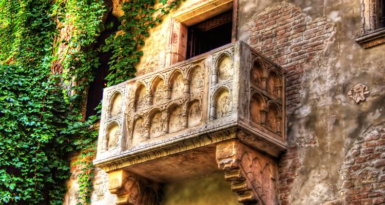 Le célèbre balcon en pierre de Juliette envahi de lierre sur une façade historique en brique à Vérone.
