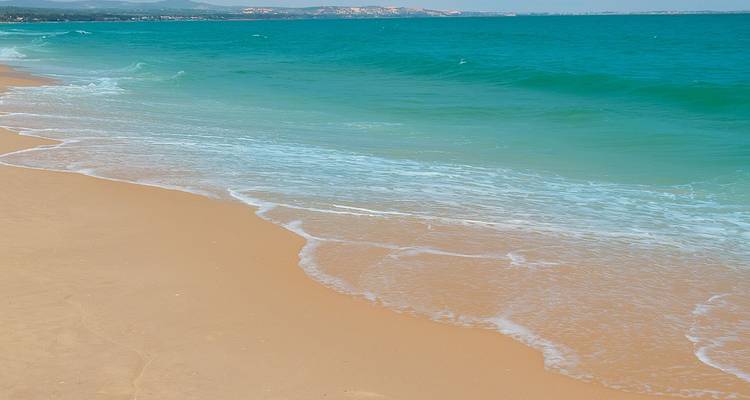 Las olas turquesas, suavemente mecidas, bañan una amplia franja de arena vacía bajo un horizonte brumoso en la costa vietnamita.