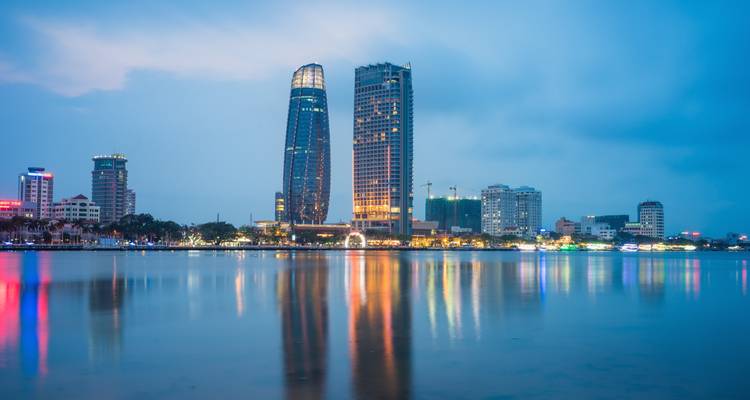 Paysage urbain avec des bâtiments modernes se reflétant dans un plan d'eau la nuit.
