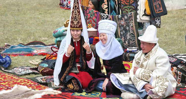 Des personnes en vêtements traditionnels kirghizes assises sur des textiles colorés.