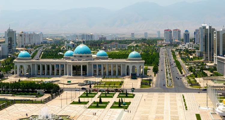 Moderne Stadtlandschaft mit blauen Kuppelgebäuden, breiten Alleen und Bergen im Hintergrund.