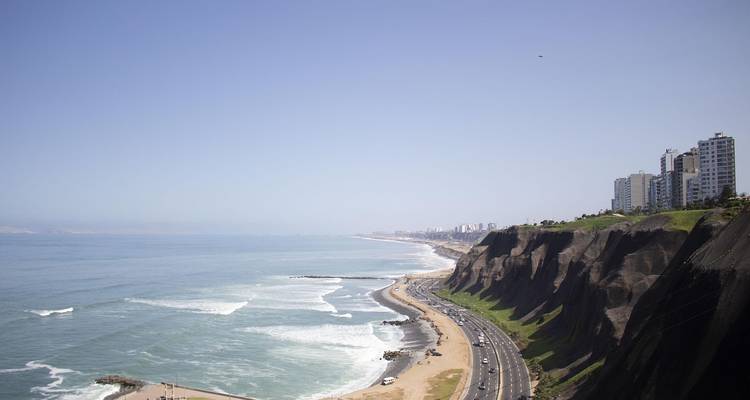 Ocean view with cliffs, a beach, and city skyline.