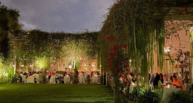 Restaurant garden with people dining under evening lights.