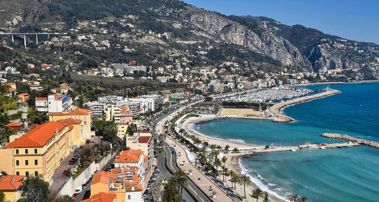 Une route côtière avec des montagnes en arrière-plan, bordée de palmiers.