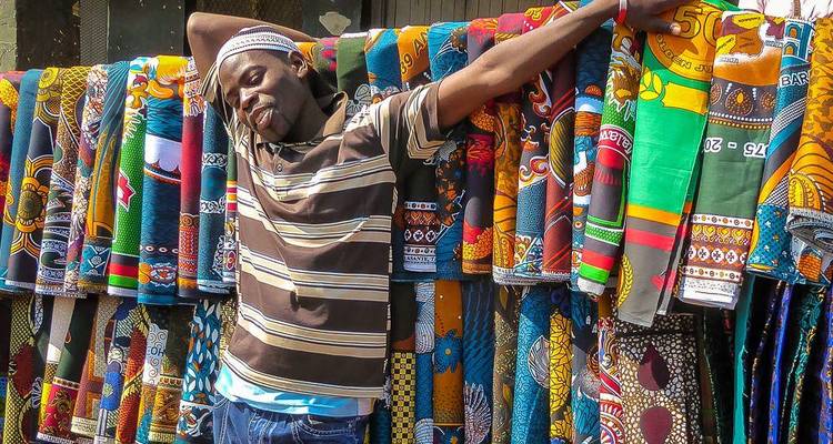 Man resting against vibrant patterned fabric in a market.