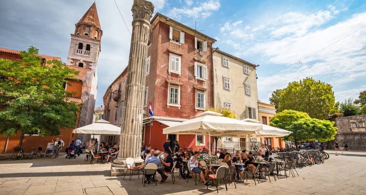 Les terrasses de cafés animées sous les anciennes colonnes et le clocher sur la place historique de Zadar lors d'un après-midi ensoleillé.