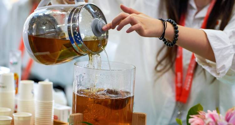 Person pouring tea from a large glass jug into a container.