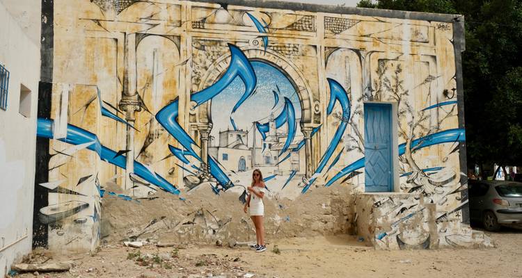 Street art on a wall with a tourist posing.
