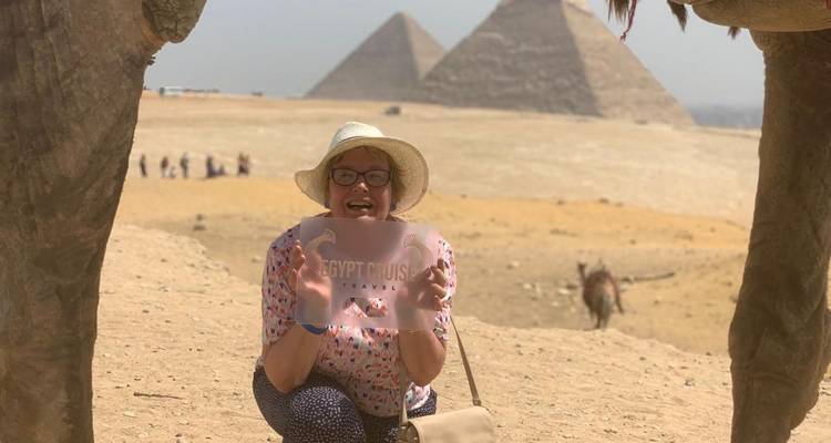 Tourist posing with a camel and pyramids in the background.