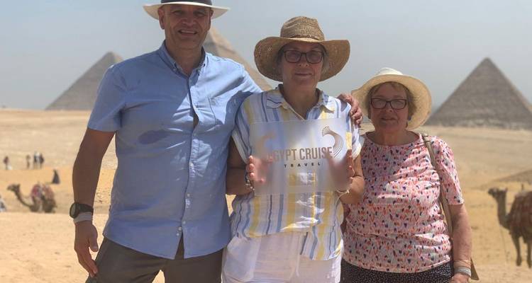 Visitors with pyramids in the background holding a sign.