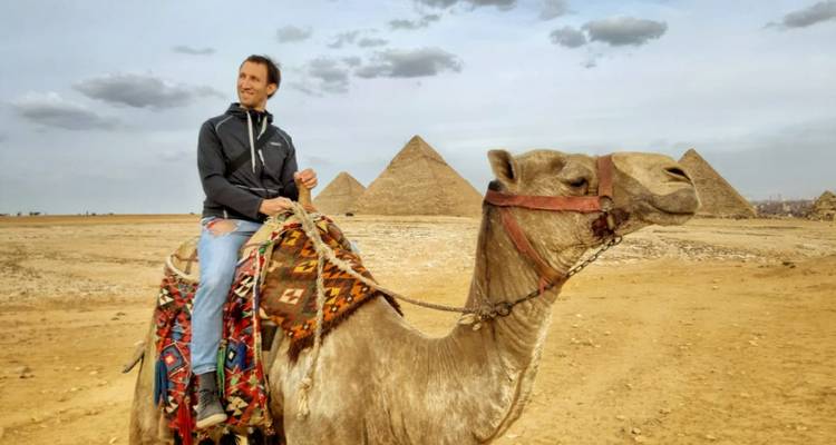 Homme montant un chameau avec des pyramides en arrière-plan.