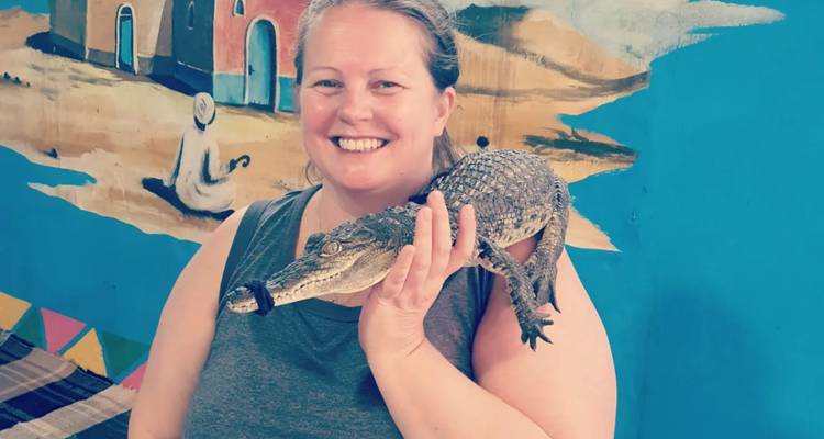 Personne tenant un petit crocodile avec un arrière-plan de peinture murale colorée.