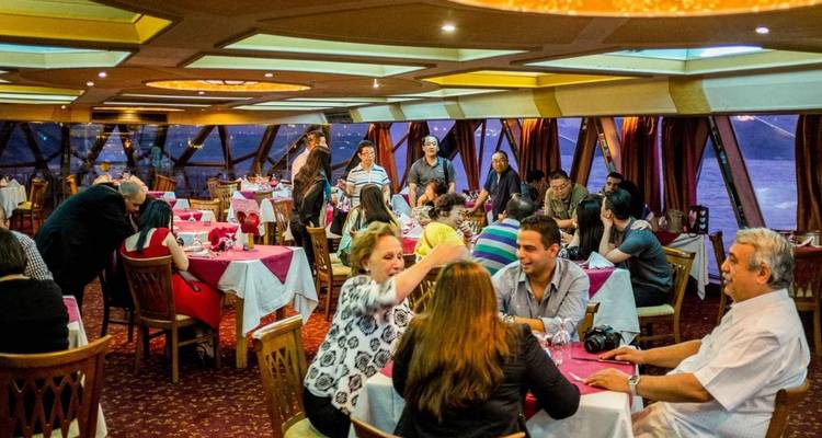 Personnes dînant à l'intérieur d'un navire de croisière avec de grandes fenêtres et une vue du soir.