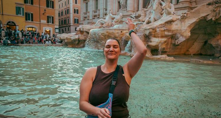 Een glimlachende reiziger poseert voor het turquoise water en sierlijke sculpturen van Rome's Trevi Fontein, midden in de beweging alsof hij een muntje gooit.
