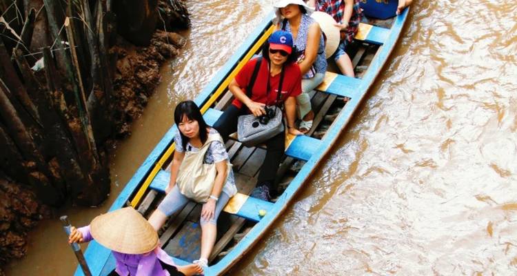 Des touristes dans un bateau naviguant à travers des eaux boueuses avec une végétation luxuriante.