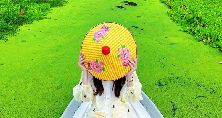 Une personne assise dans un bateau tenant un chapeau décoratif sur un plan d'eau vert.