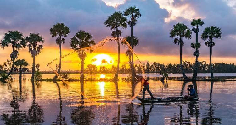 Des pêcheurs lançant un filet au coucher du soleil avec des palmiers en silhouette.
