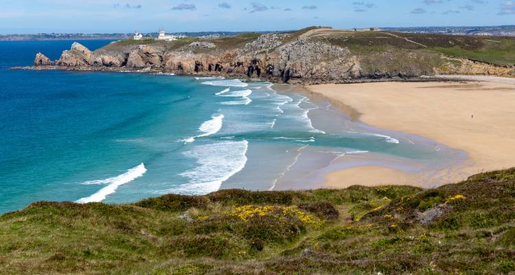 Paysage côtier avec une plage de sable et des falaises rocheuses.